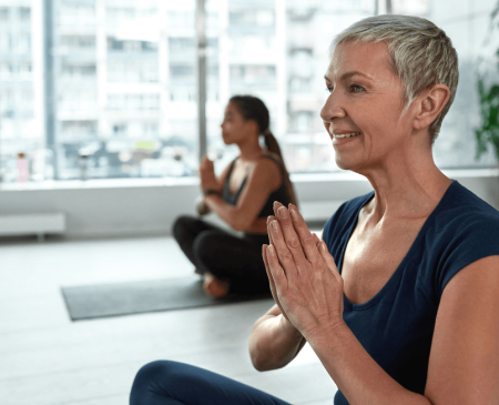 Smiling Woman Over 50 Practising Yoga At Gymplus, Highlighting The Benefits Of Exercise For Women 50+ For Fitness, Flexibility, And Well-being.