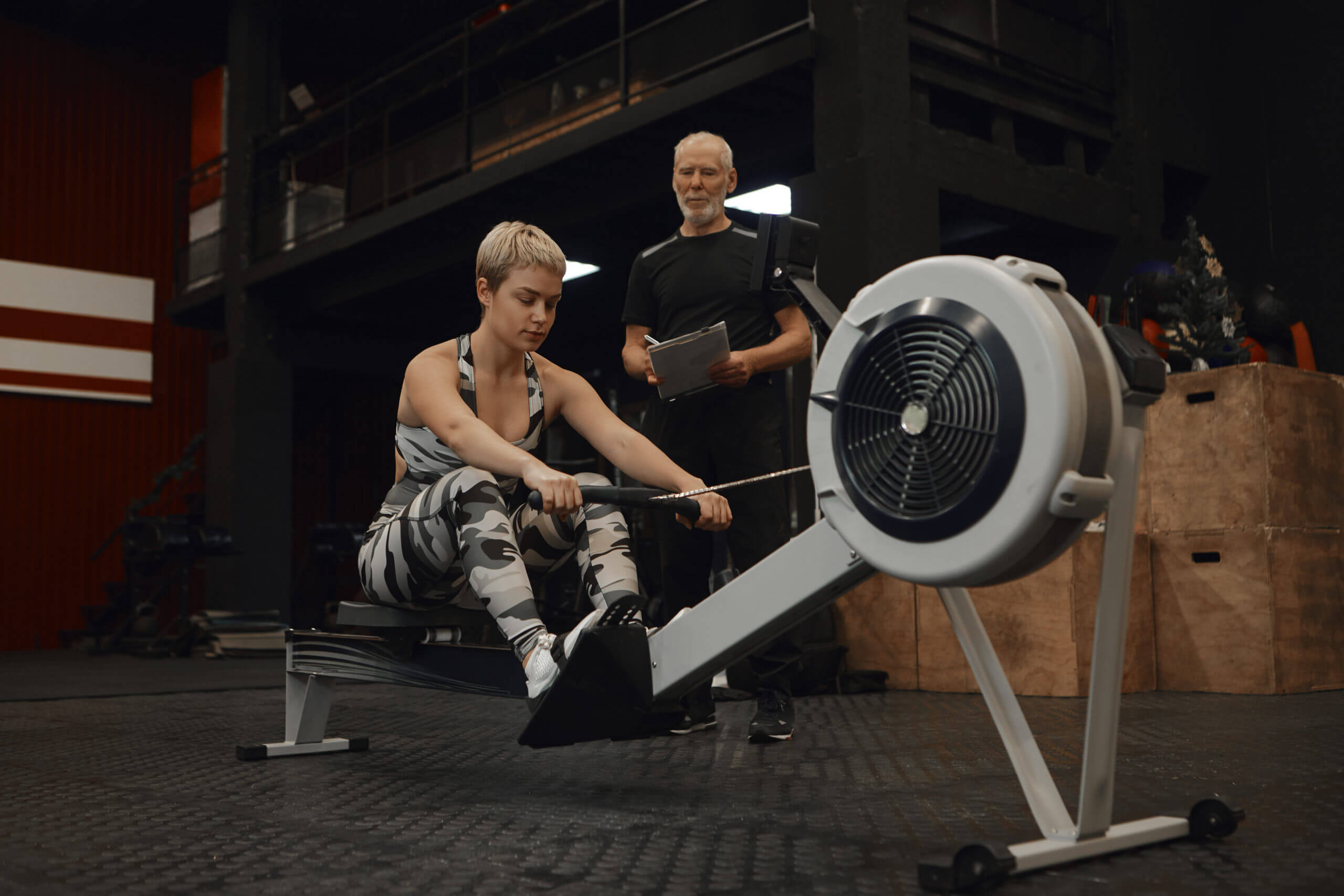 https://gymplus.ie/wp-content/uploads/2022/07/picture-senior-bearded-male-fitness-insturctor-with-clipboard-watching-his-female-client-exercise-rowing-machine-attractive-woman-training-gym-with-personal-coach-doing-cardio-workout-scaled-1.jpg