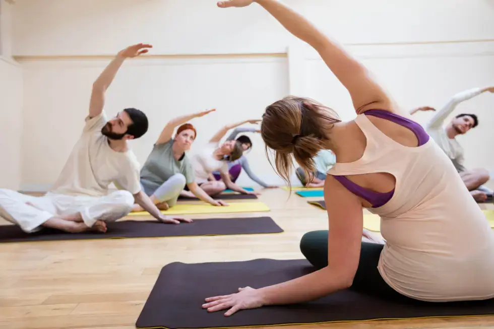 Group yoga class stretching on mats at Gym Plus, focusing on flexibility and mindful movement in a calm studio environment.